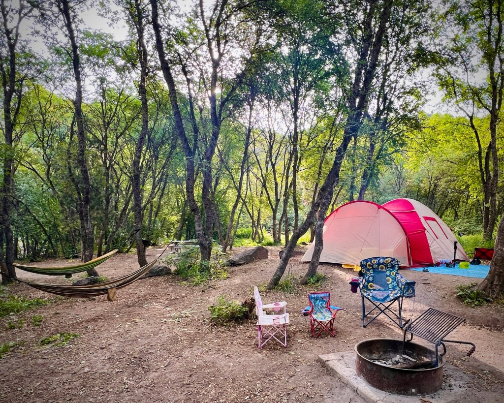Erdei sátortáborhely egy rózsaszín sátorral, színes gyerekszékekkel, tábortűzrakó hellyel és függőággyal – ADHD-s családi kikapcsolódás kezdete.